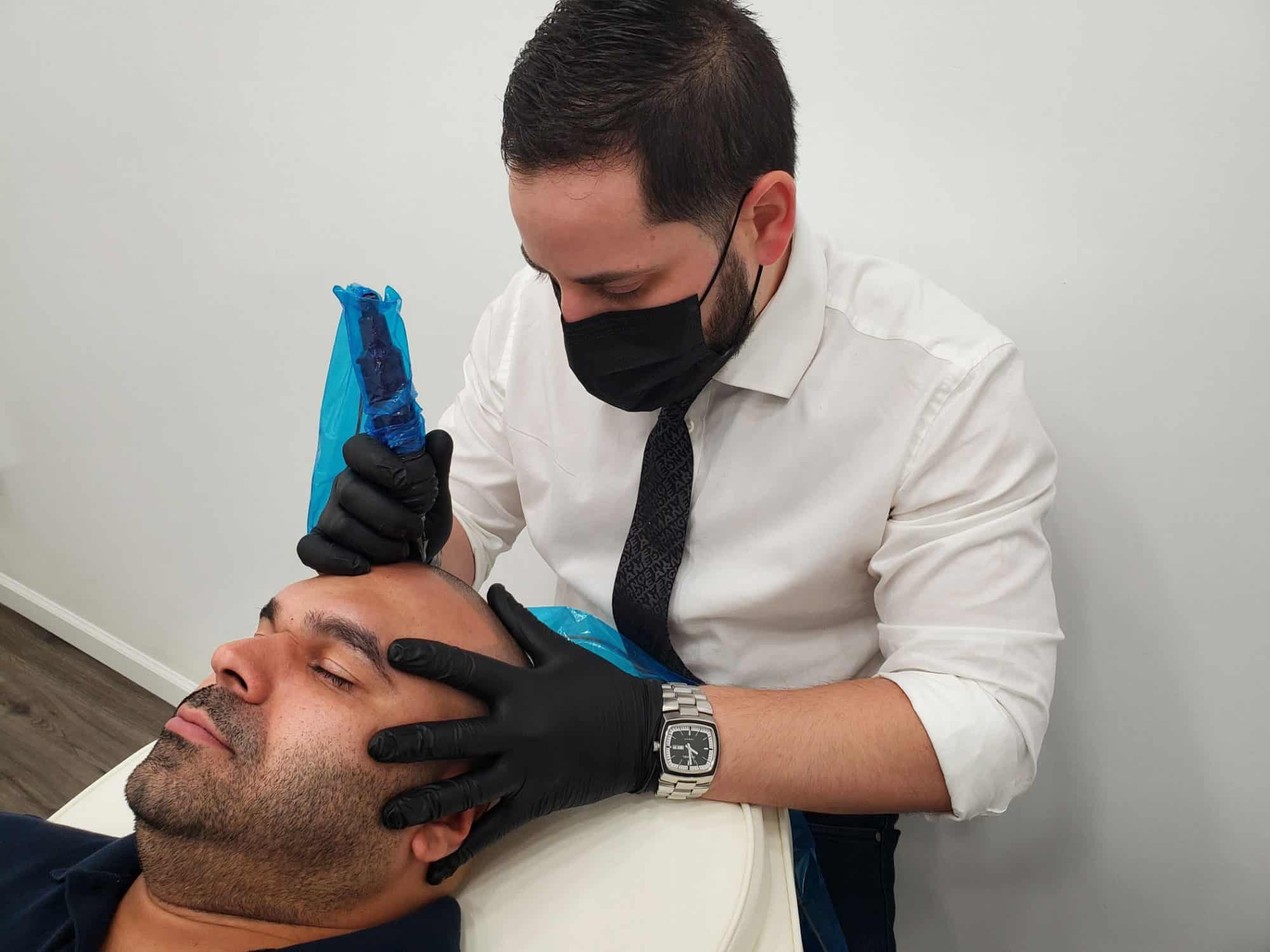 Erik Lorenzo performing a scalp micropigmentation treatment on a client at Artisan Scalp Micropigmentation